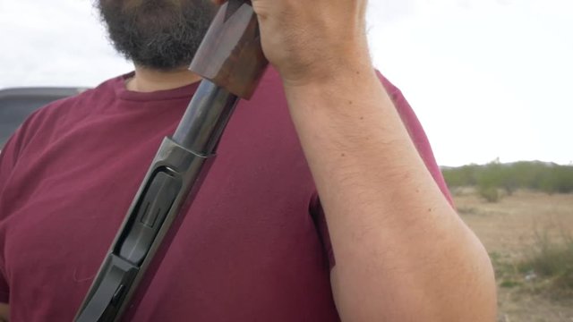 Handsome bearded man loading ammo shells into a shotgun in slow motion. The overweight hunter loads shotgun cartridges into the barrel of his firearm. Closeup shows social issues & civilian militias.
