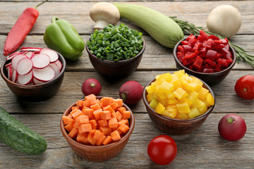 Fresh sliced vegetables in bowls on wooden table