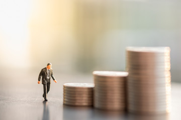 Money, Financial, Business Growth concept. Businessman miniature figure walking to stack of coins under sunlight.