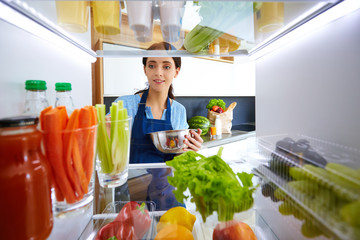 Portrait of female standing near open fridge full of healthy food, vegetables and fruits. Portrait of female