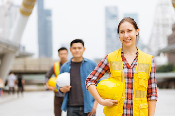 Portrait of young engineer girl, posing outdoor with team and construction on background