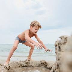 Cute little boy building with sand on the background of sea, image with square aspect ratio