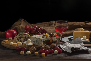 Different kinds of cheeses, red grapes and wine in glass, snack on wooden, rustic table. Still life, cheese plate, top view.