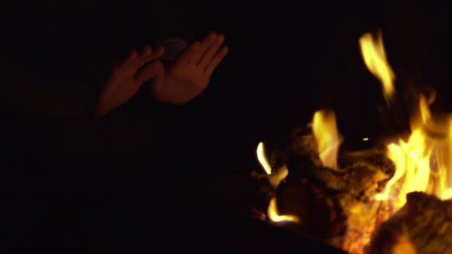 Unrecognizable woman warming her hands near a campfire at night. Locked down real time close up shot