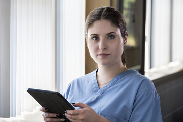 Portrait of a female health professional reading information on a tablet in window light