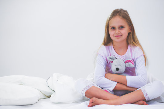 Little girl in the bedroom is sitting on the bed. Little girl is wearing a pajamas and sitting in bed .