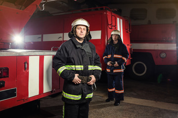 Fototapeta premium Strażak (strażacy) w akcji stojący w pobliżu wozu strażackiego. Bezpieczeństwo awaryjne. Ochrona, ratowanie przed niebezpieczeństwem.