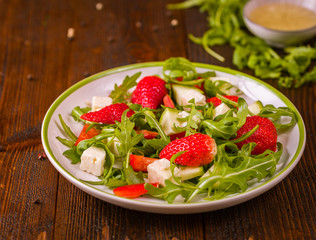 Fresh vegetable strawberry salad on white plate on natural rustic desk.