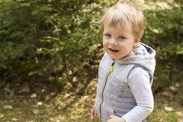 Beautiful little blonde hair boy with open mouth, happy eyes in the spring forest. Child portrait. Creative concept. Summer time. Close up
