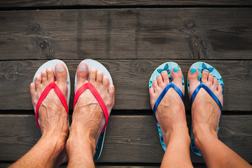 Man and woman feet in flip-flops standing on wooden deck.