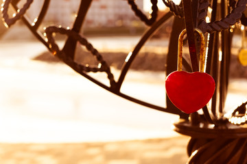 Sunlit red padlock in shape of a heart, selective focus.