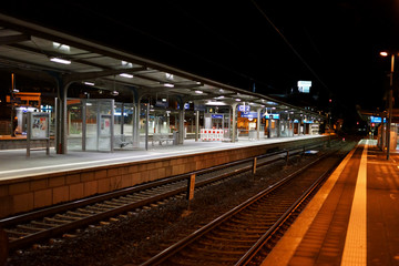 Fototapeta premium Bahnsteig mit Nachtbeleuchtung / Der Bahnsteig des Bahnhofes Weinheim in der Nacht mit Sitzplätzen, Schienen und Glasunterständen.