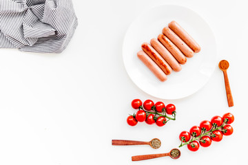 Grilled sausages on white table near cherry tomatoes and spices in wooden spoons top view copy space