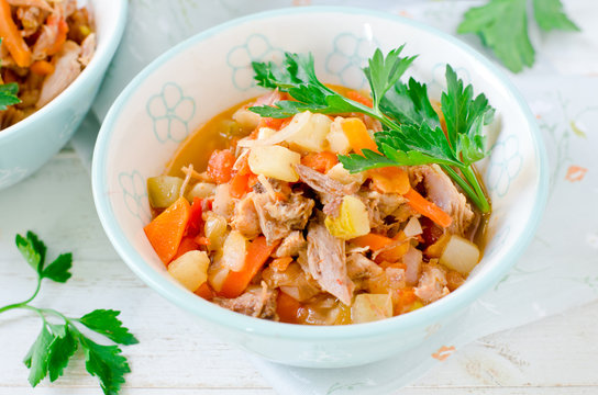 Stew of turkey and vegetables (zucchini, onions, carrots, tomatoes, bell peppers) on a white wooden table