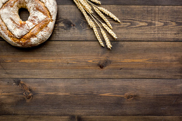 Home bread with classic recipe. Round loaf near ears of wheat on dark wooden background top view copy space