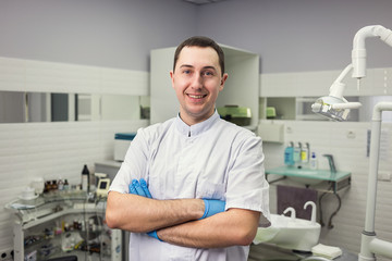 Obraz premium Male dentist standing with his hands crossed over medical office background. Healthcare, profession, stomatology and medicine concept
