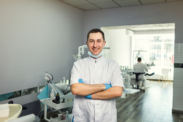 Obraz premium Male dentist standing with his hands crossed over medical office background. Healthcare, profession, stomatology and medicine concept