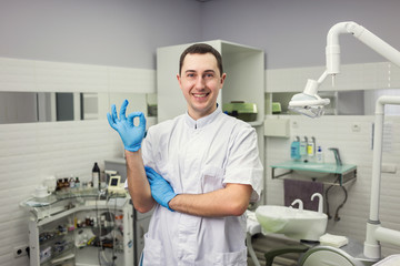 Male dentist standing over medical office background. Healthcare, profession, stomatology and medicine concept