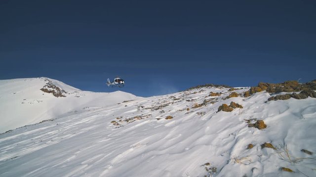 The heliskiing helicopter landed in the mountains in winter, raising a cloud of snow