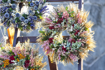3 beautiful flower wreaths displayed on the wooden stand shortly after sunrise. Street market at...