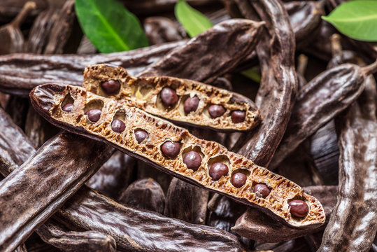 Carob pods and carob beans on the wooden table.