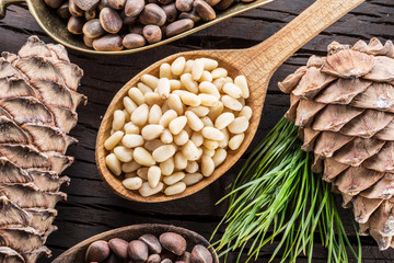 Obraz premium Pine nuts in the spoon and pine nut cone on the wooden table. Organic food.
