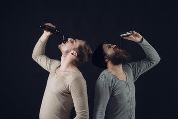 Company of dirty friends spend leisure with drinks. Men on drunk faces, dark background. Guys hold bottle and flask with alcohol,drinking. Alcohol addict concept. Alcohol, addiction, leisure.
