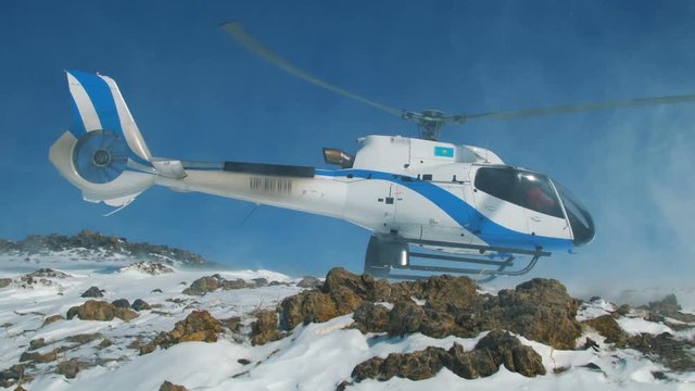 Helicopter landed in the snow mountains, raising a big cloud of snow
