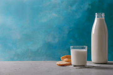 Glassware with milk and bread on table against color background