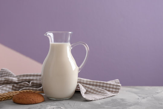 Jug of fresh milk and cookie on table against color background