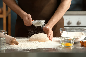 Obraz na płótnie Canvas Man sprinkling flour over dough on table in kitchen