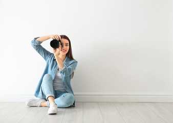 Female photographer with camera sitting on floor near wall indoors