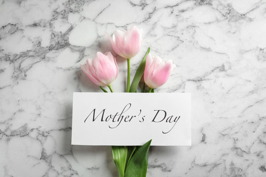 Beautiful tulips and greeting card with words "Mother's Day" on marble background, top view