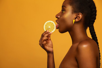 Cheerful young african woman with yellow makeup on her eyes. Female model against yellow background...