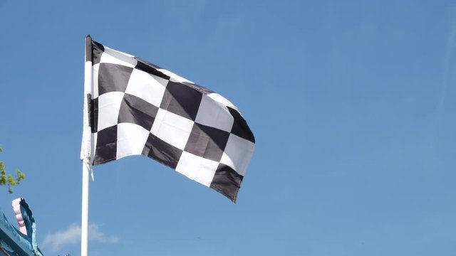 Checkered racing flag shake in the air in the blue sky background.