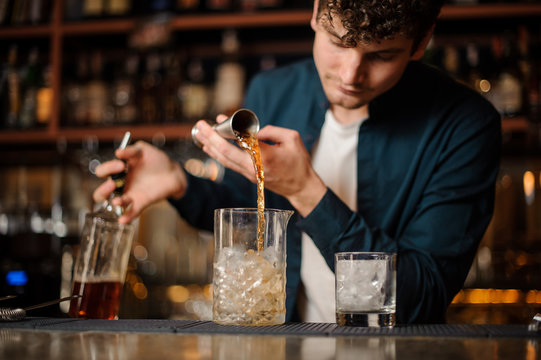 Curly barman pouring sweet syrup into a jar with ice making an alcoholic drink