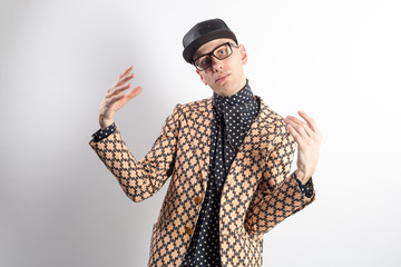 Slim elegant man in a black cap and stylish suit looking at the camera with funny gesture. Isolated on white.