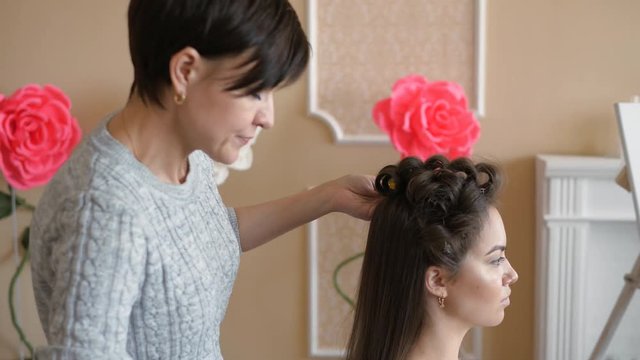 Makeup artist stylist works with model. hairdresser does the hair styling of the model. woman is working a styler with the girl's long hair. The hairdresser makes curls on the girl's straight hair