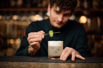 Bartender decorating a cocktail glass with a cucumber on a wooden skewer