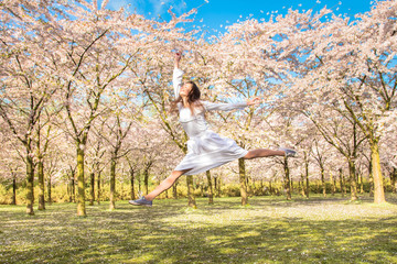 Happy teenager he is laughing and jumping up in blossoming cherry blossoms.