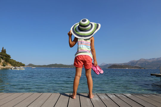 little girl in big hat enjoy on the beach and sunbathe in the sea resort