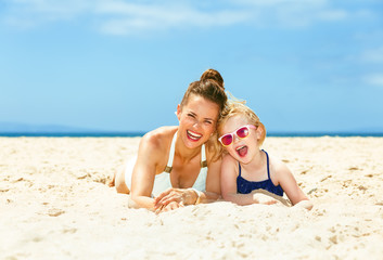 happy young mother and child in swimsuit laying on seacoast