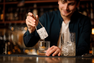 Bartender putting a big ice cube into an empty glass