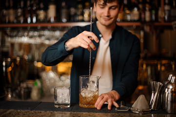 Brunet bartender stirring an alcoholic drink in the glass with ice