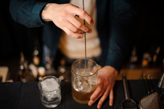 Brunet bartender stirring an alcoholic drink in the measuring glass with ice