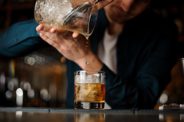 Bartender pouring an alcoholic cocktail into a glass with a big ice cube