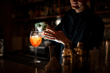 Brunet bartender adding an alcoholic drink into a glass with a cocktail