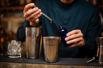 Bartender adding an essence to a steel shaker with an alcoholic cocktail