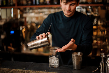 Bartender pouring an alcoholic cocktail into a glass from a steel shaker