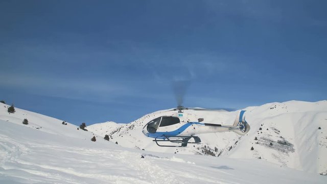 The helicopter takes off and flies away against the background of the snow mountains